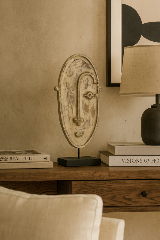 Decorative mask on a wooden surface with books and a lamp in the background