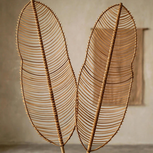 Two large woven raffia or palm leaf wall hanging decorations with long bamboo stakes, displayed against a neutral textured plaster wall.