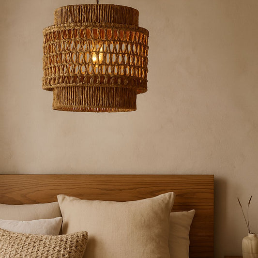 Woven pendant light fixture above a wooden headboard with pillows on a beige wall.
