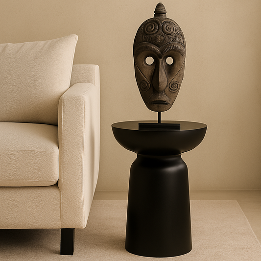 African mask on a black pedestal in a room with a beige sofa and wall.