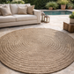 Round woven rug on a stone patio with a beige sofa and outdoor setting.