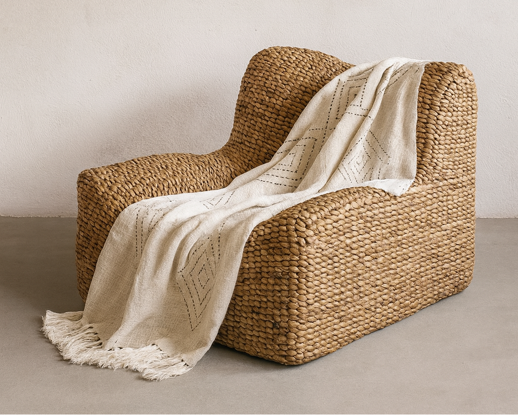 Woven chair with a white blanket draped over it against a plain wall.