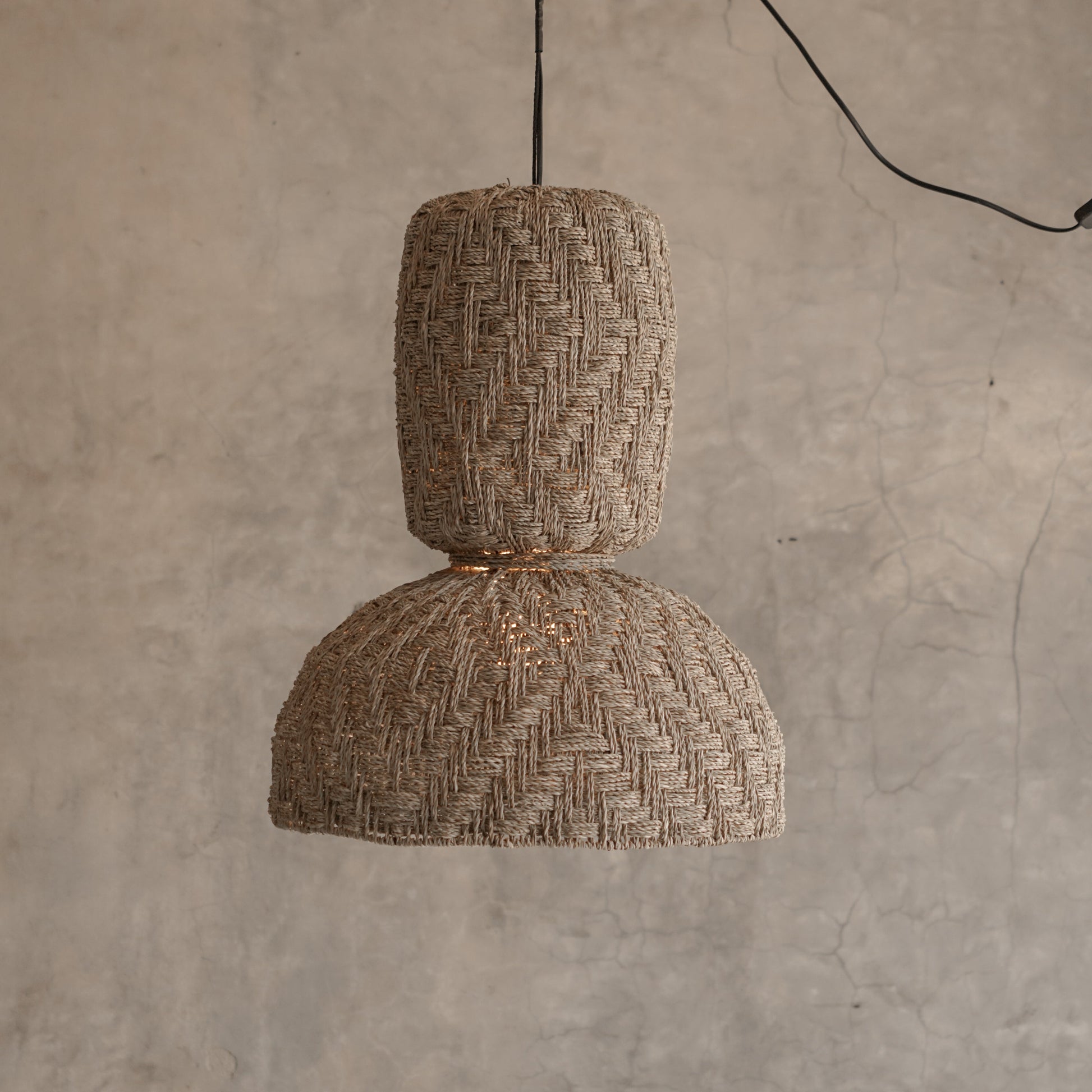 Woven pendant light hanging against a textured wall.