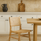 Wooden chair and table in a kitchen setting with beige tiles and white cabinets.