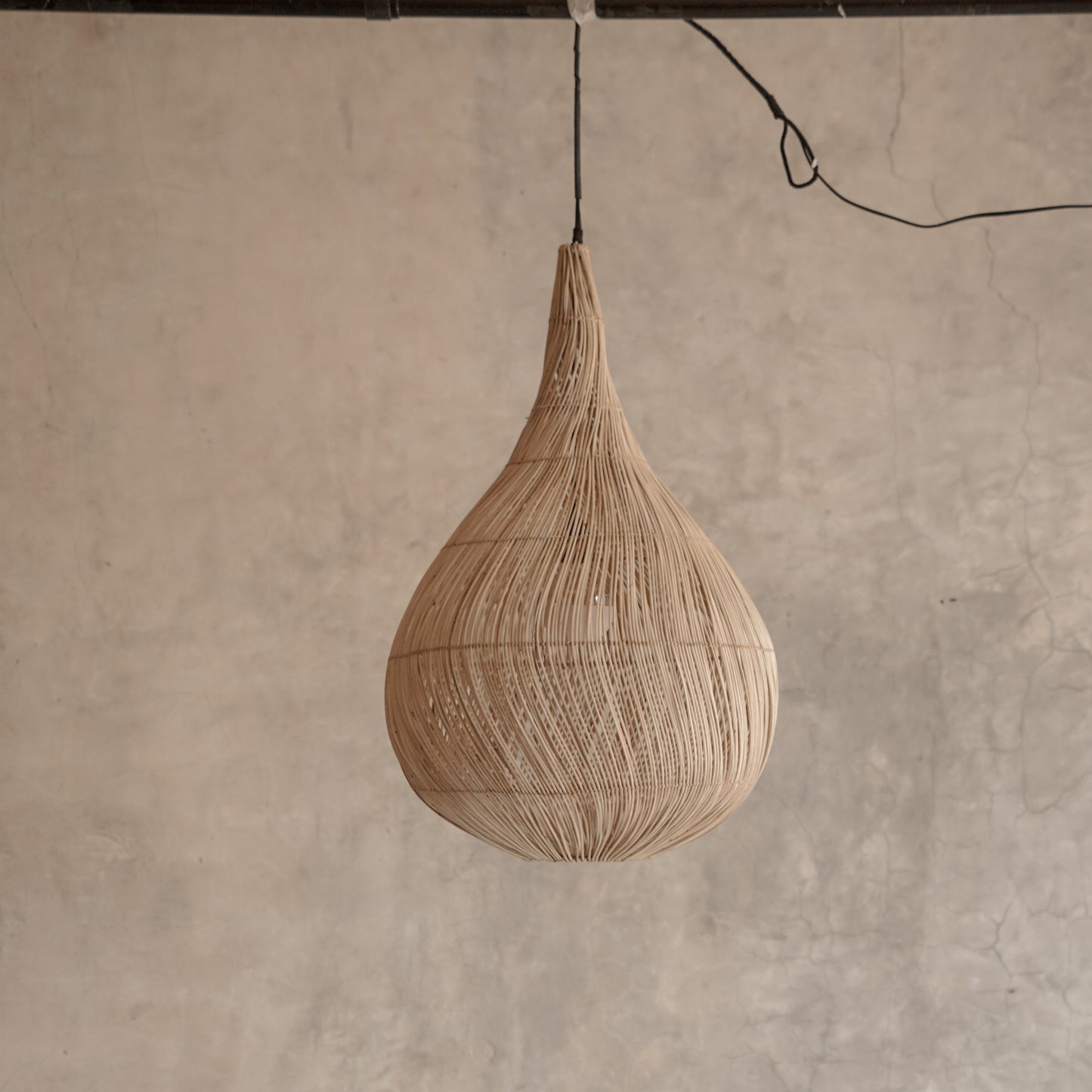 Woven pendant light hanging against a textured wall.