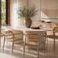 Dining room with a long white table and wooden chairs, featuring a vase with greenery on the table.