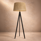Floor lamp with a beige shade and black tripod base against a beige wall.