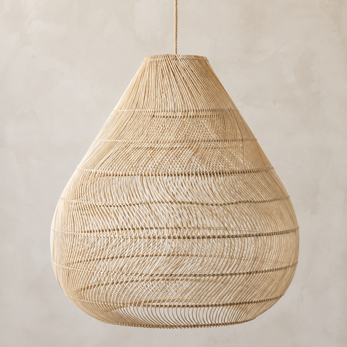 A teardrop-shaped woven pendant light made from natural beige raffia or wicker, suspended by a thin cord against a textured beige plaster wall.