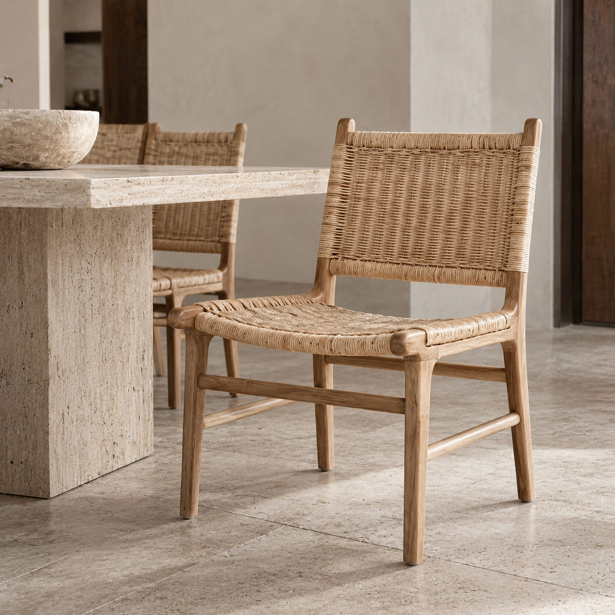 A natural woven rattan dining chair with a light wood frame, shown in a modern dining room setting next to a stone table.