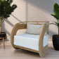 A beige rattan chair with a cushion and a decorative pillow, placed in a room with a light interior, surrounded by plants.