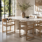 Round marble dining table with wicker chairs in a bright room with large windows.
