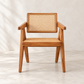 A mid-century modern wooden armchair with a woven cane backrest and seat, shown against a neutral textured beige wall and floor.