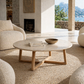 Modern living room with beige armchairs, a round wooden coffee table, and a scenic view.