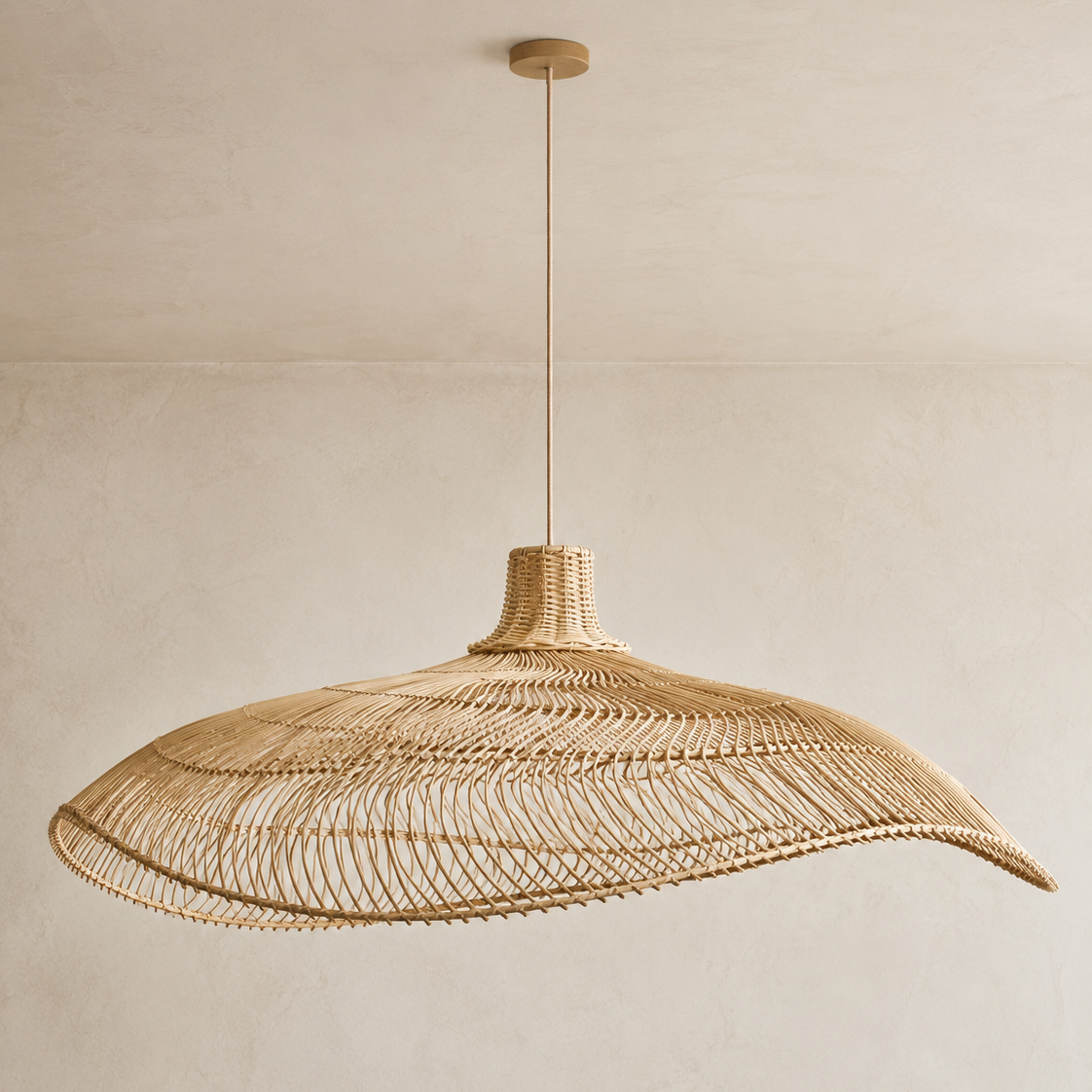 A large woven pendant light made of natural rattan or wicker, suspended from a thin rod against a warm beige plaster wall and ceiling.