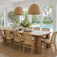 Dining area with wooden table and chairs in a bright room with large windows.