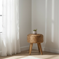 Wicker side table with a plant in a room with white curtains and light-colored floor.