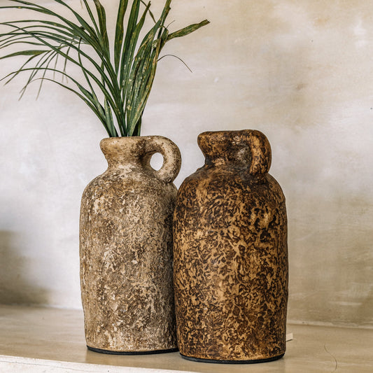 Two brown terracotta vases with a textured surface, displayed against a neutral background with a green plant.
