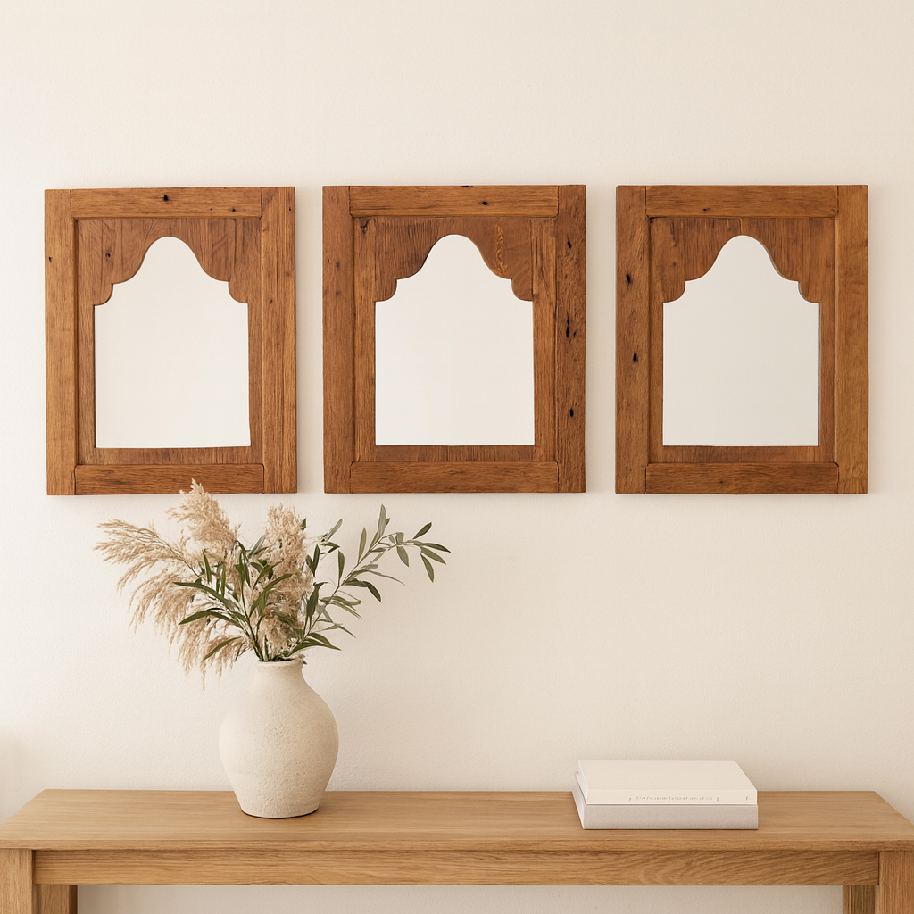 Three wooden mirrors on a wall above a wooden table with a vase and book.